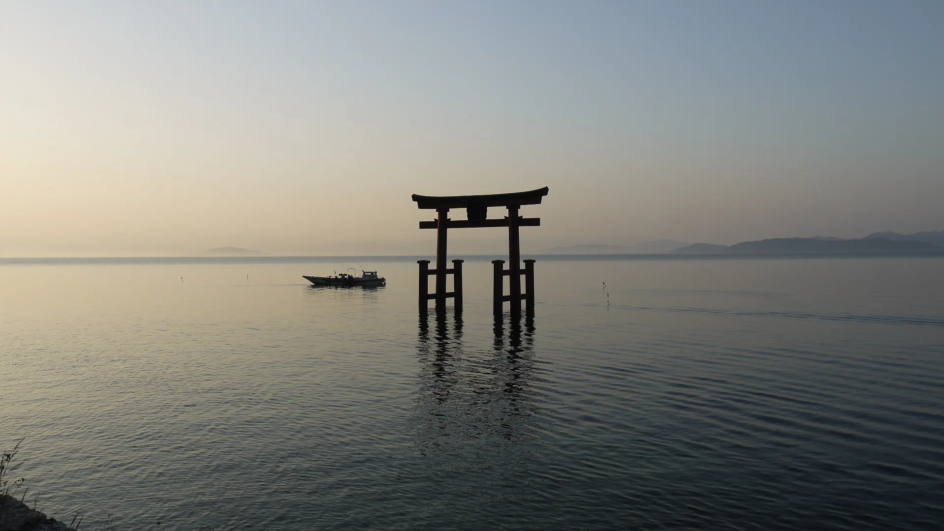 朝の静かな湖面に立つ鳥居と小舟